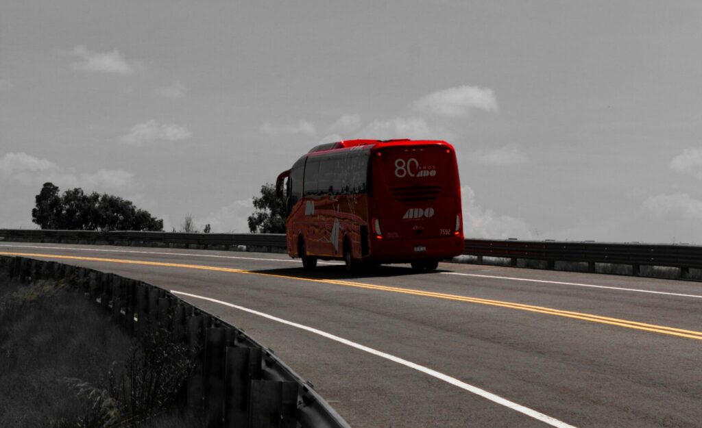 A red bus driving down a highway under a cloudy sky